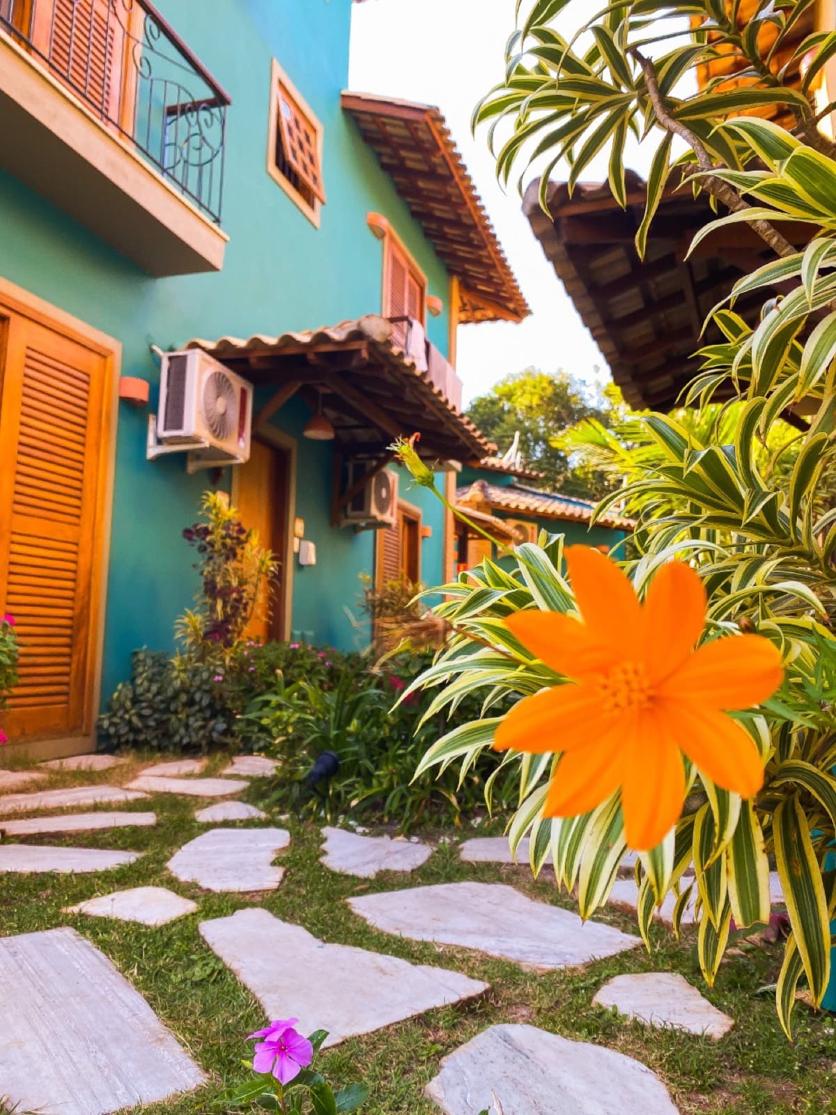 Fachada do chalé azul com caminho de pedras, jardim tropical e flor laranja