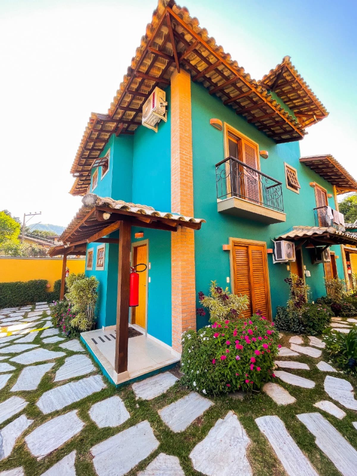 Fachada do chalé turquesa de dois andares com varanda de ferro e jardim