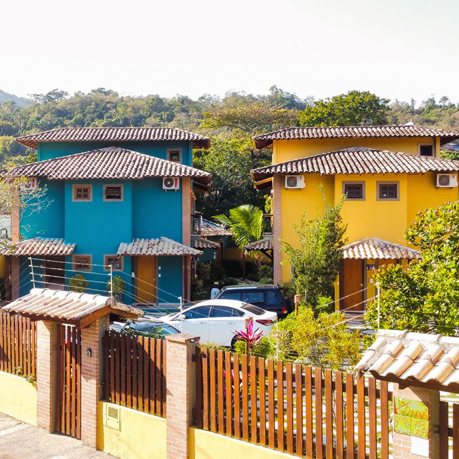 Os chalés azul e amarelo com telhado colonial, cercados por verde e morros