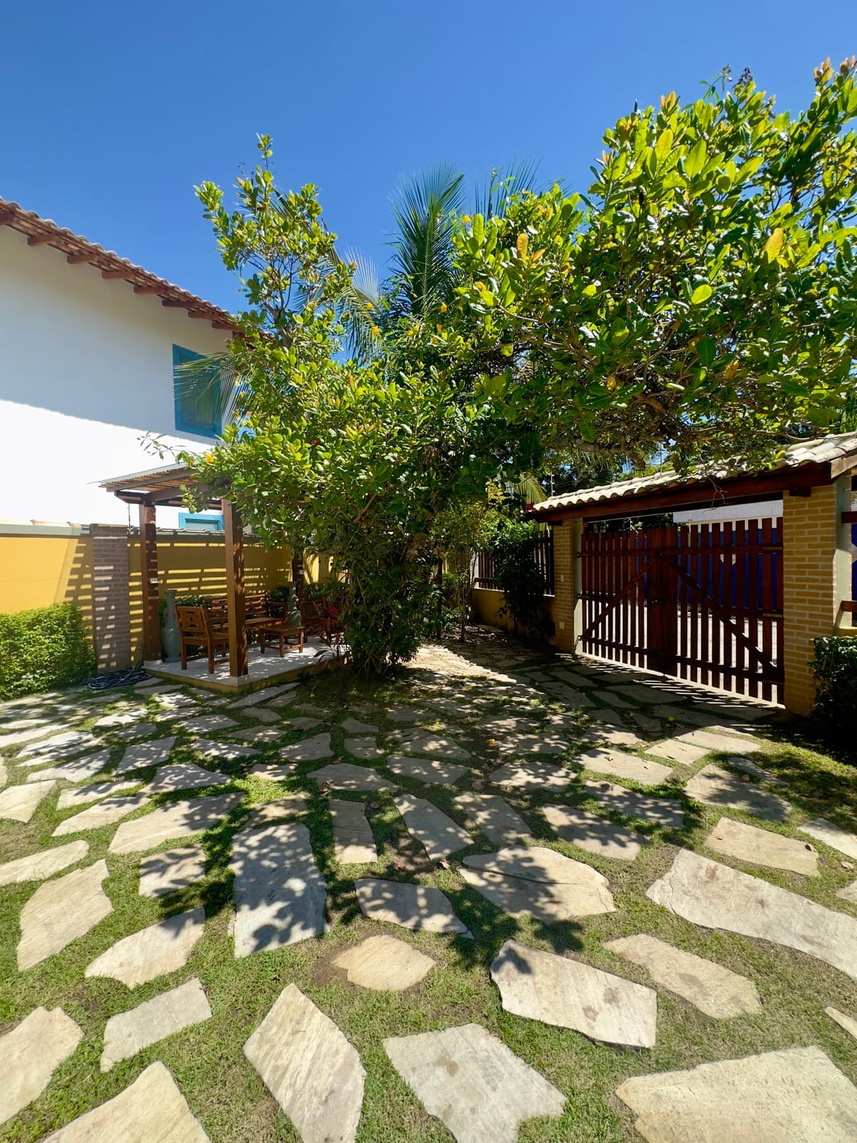 Jardim com pergolado, área de estar e grande árvore de sombra