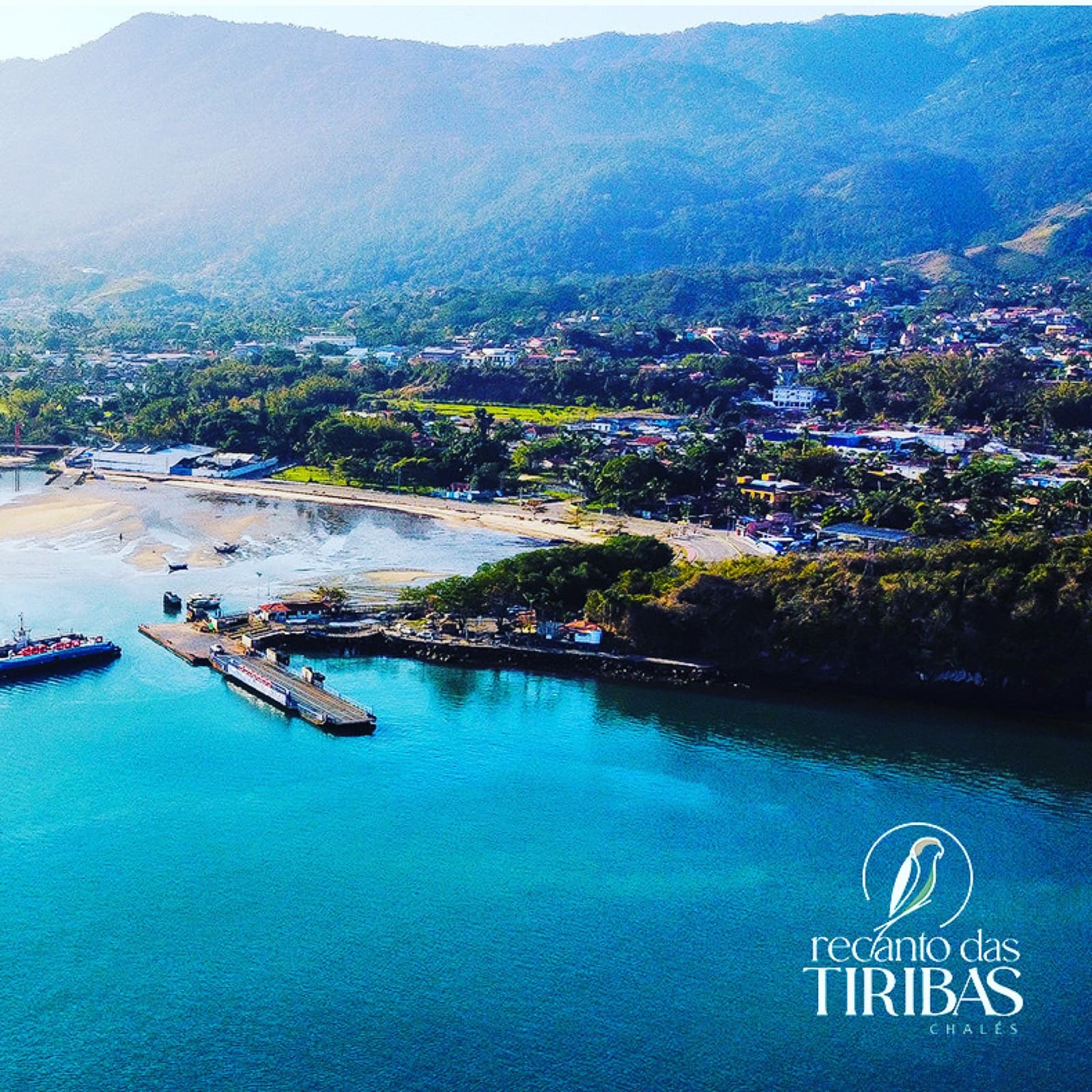 Vista aérea da orla de Ilhabela com água turquesa, píer da balsa e montanhas