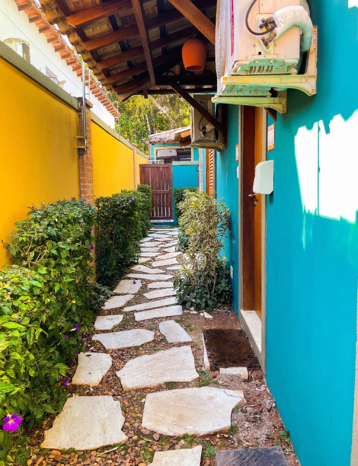 Caminho de pedra entre as paredes coloridas dos chalés, com canteiro de plantas
