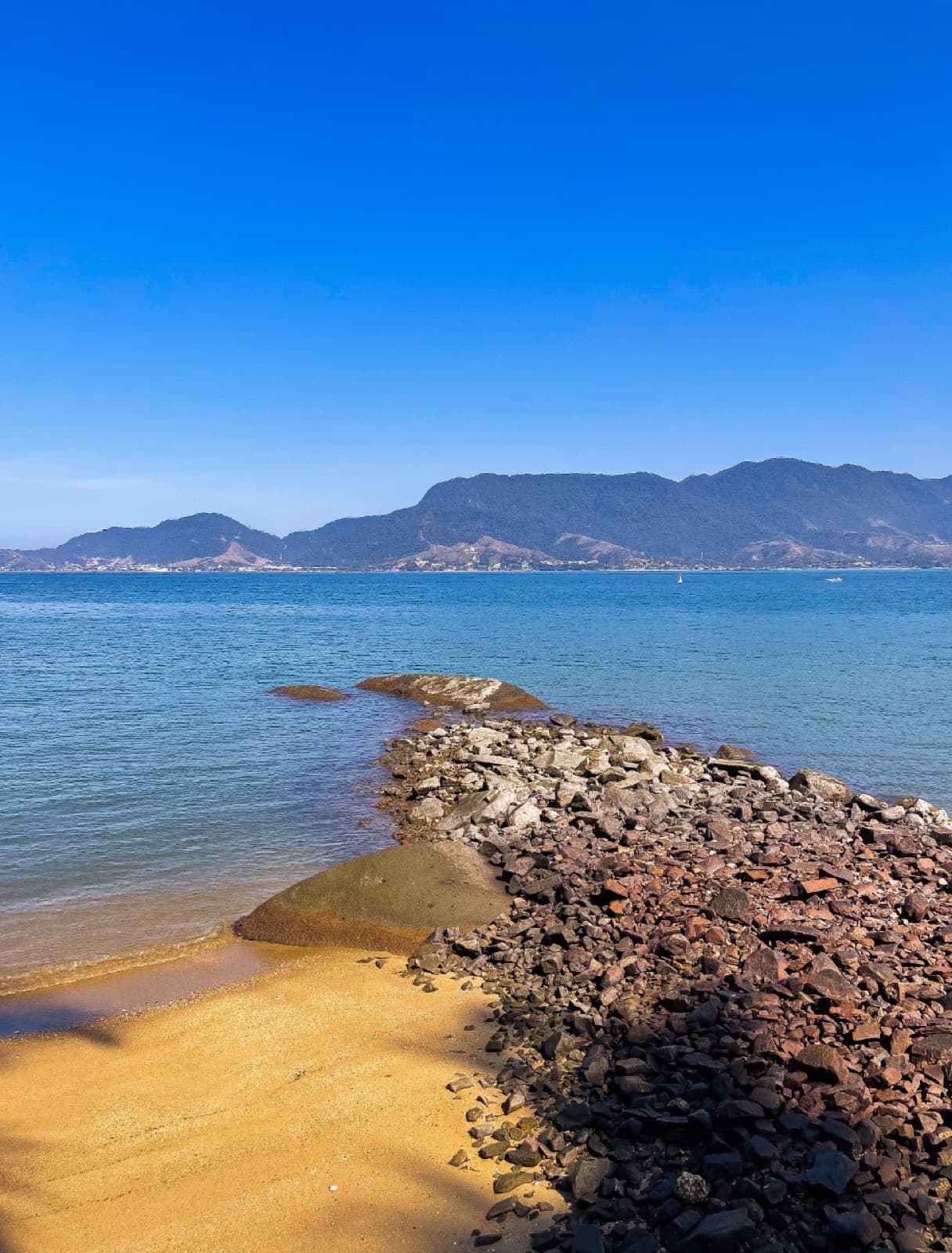 Prainha de areia dourada com água azul clara e montanhas ao fundo