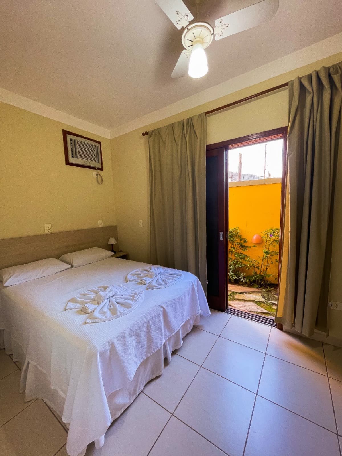 Quarto com cama de casal, ventilador de teto e porta de vidro pro pátio