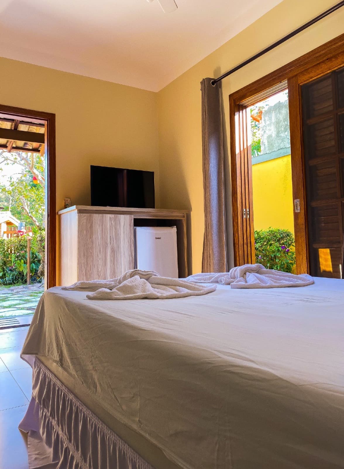 Quarto com cama de casal, toalhas dobradas, TV e frigobar